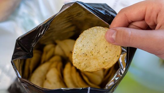 Mann, greift in eine Chipstüte.