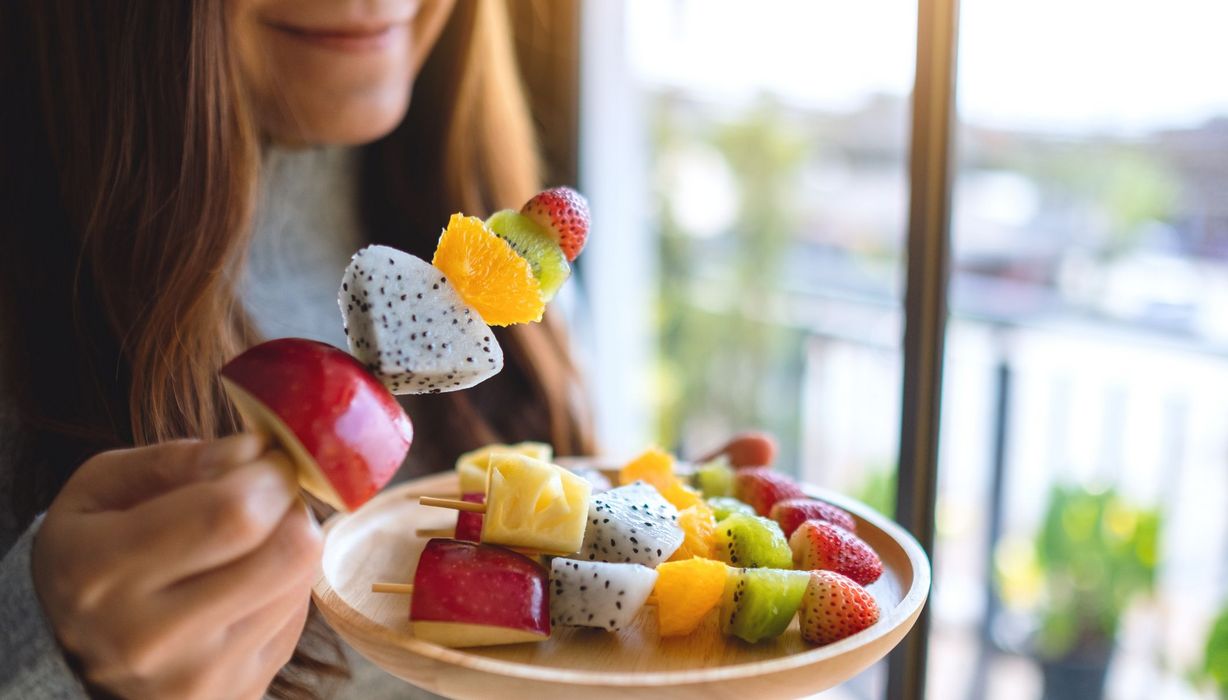 Frau, isst frisches Obst an einem Spieß.