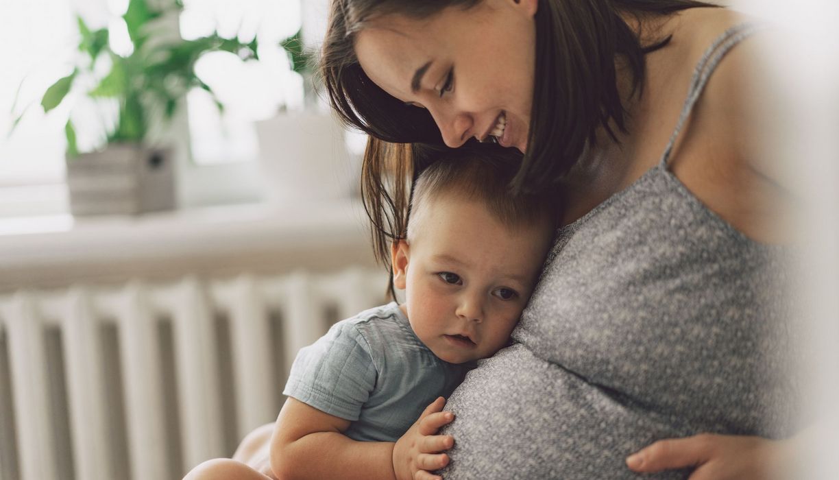 Kleinkind, kuschelt sich an den Bauch seiner schwangeren Mutter.