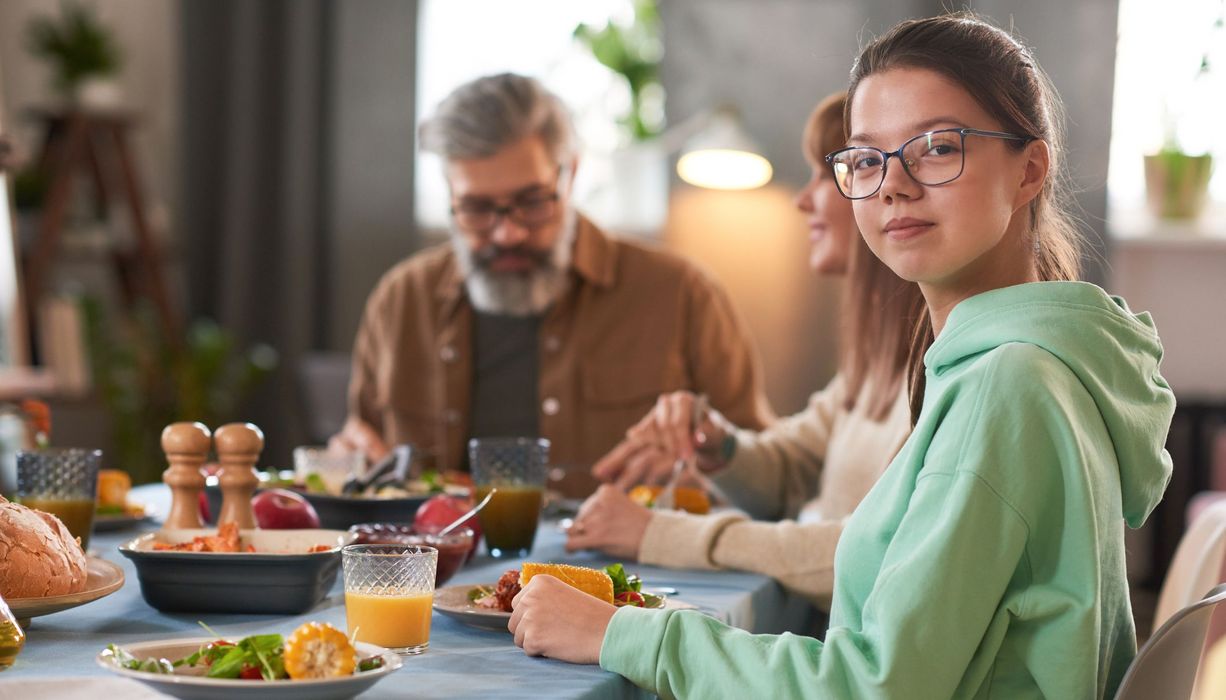 Teenager, sitzt mit der Familie gemeinsam am Tisch und isst.