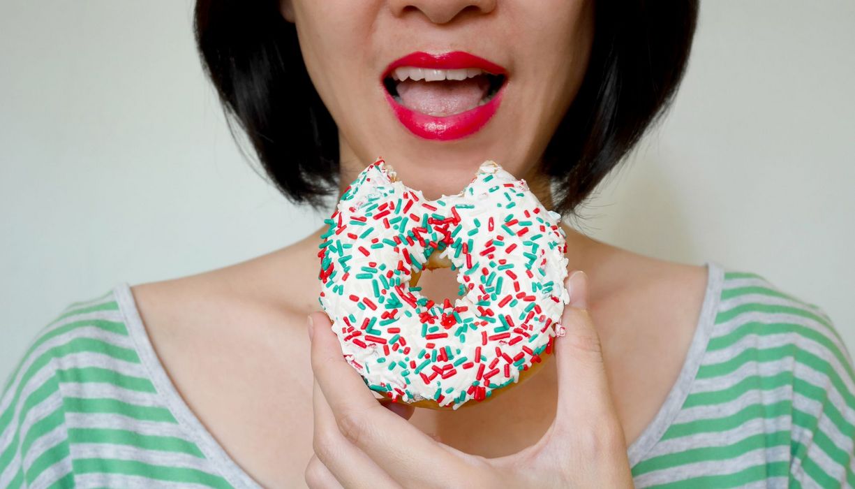 Frau, beißt in einen Donut mit bunten Streuseln.