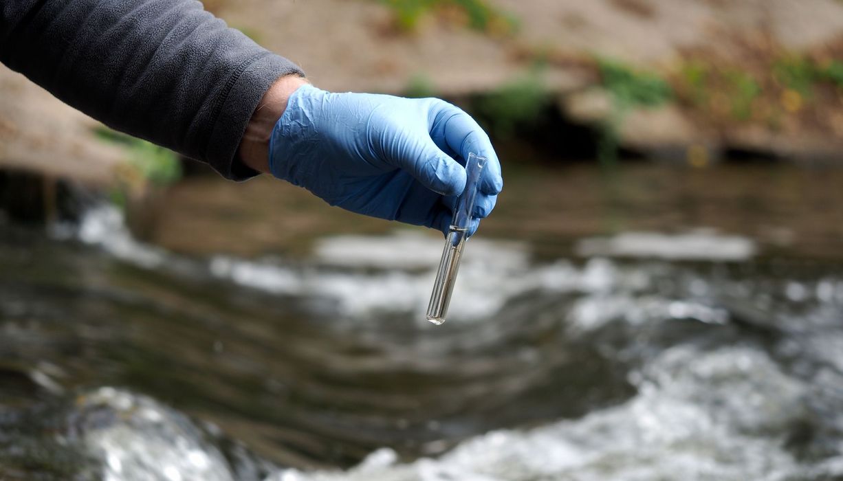 Mensch, holt eine Wasserprobe aus einem Gewässer.