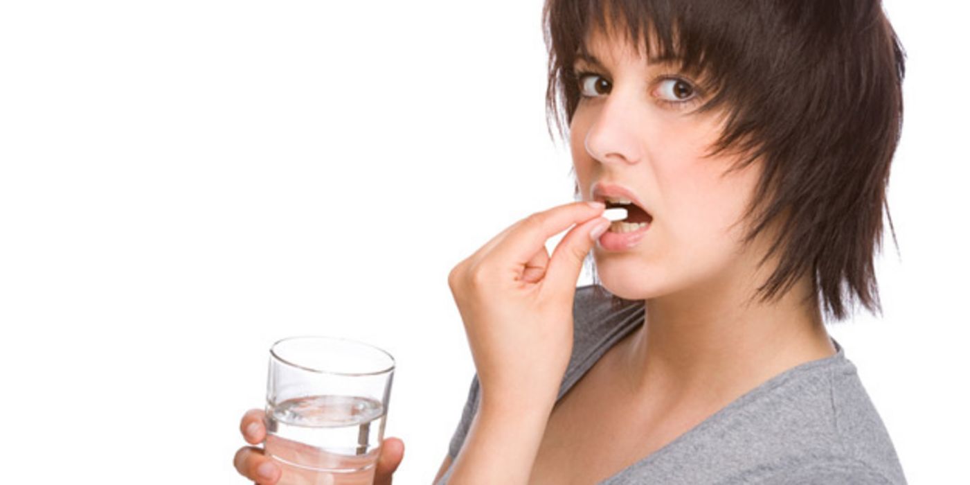 Junge dunkelhaarige Frau bei der Einnahme eines Medikaments, in der Hand ein Wasserglas