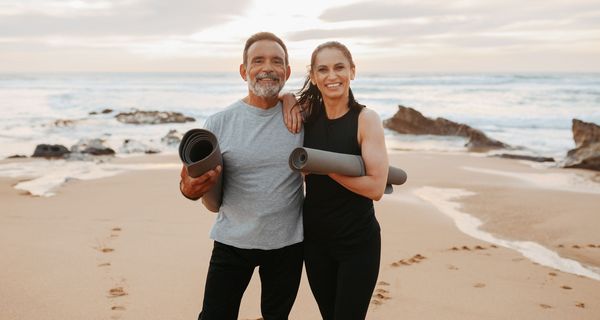 Zwei glückliche und sportliche ältere Menschen am Strand mit einer Gymnastikmatte. 