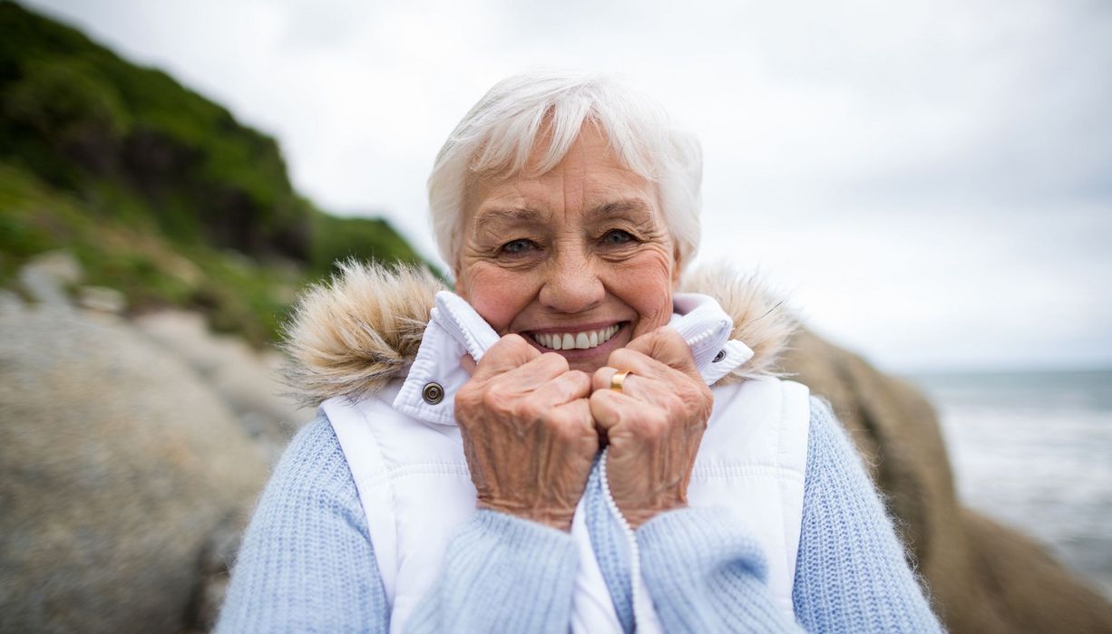 Ältere Dame mit warmer Kleidung am Strand, winterlich.