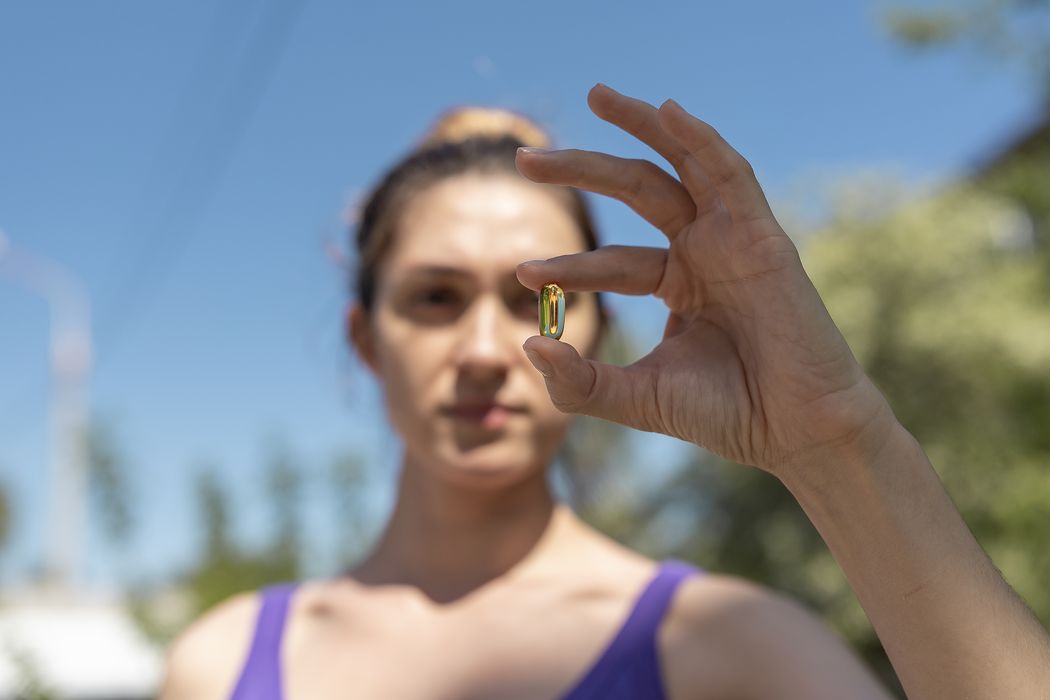 Frau, hält eine Vitamin D-Pille in der Hand.