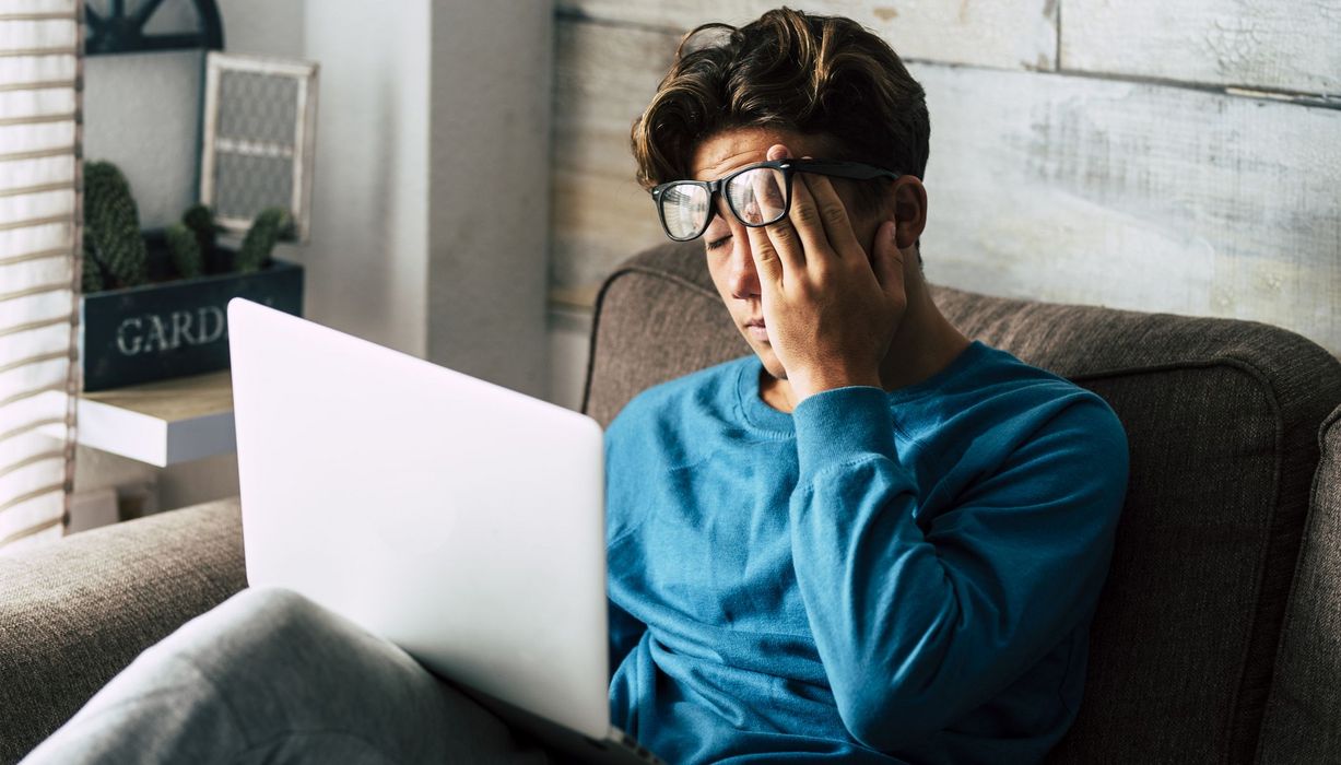 Junger Mann, müde mit Laptop auf der Couch.