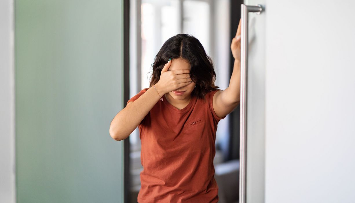 Frau, hält sich an einer Wand fest.