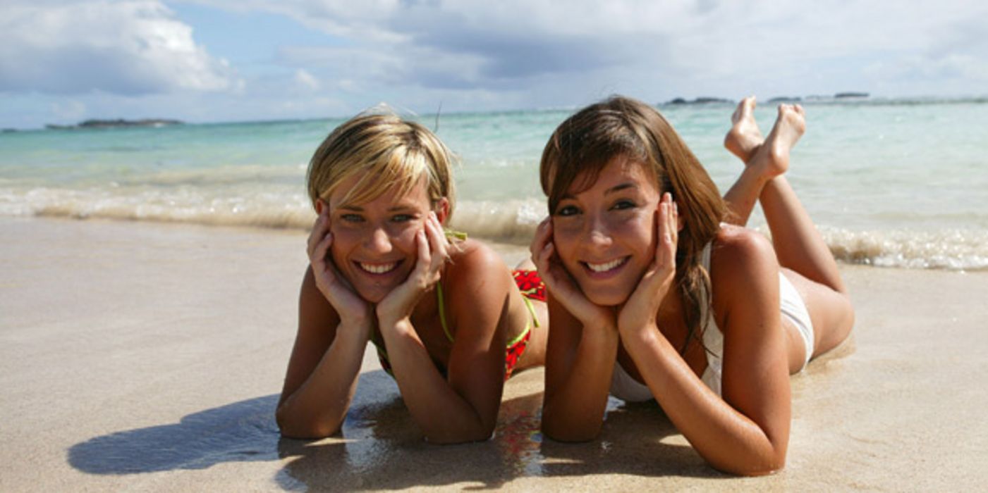 Zwei Frauen liegen am Strand in der Sonne.