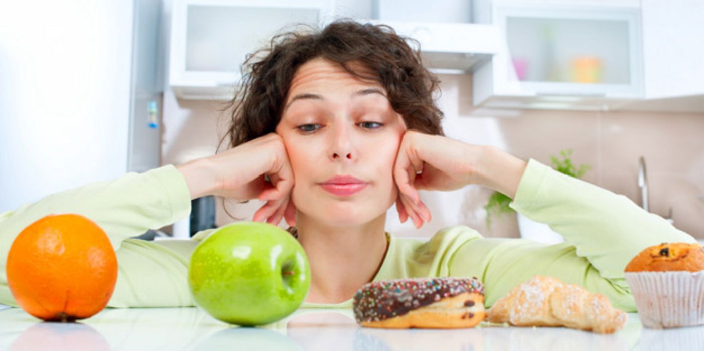 Frau, vor der Orange, Apfel, Donut, Croissant und Muffin aufgereiht sind und die unglücklich auf den Apfel blickt