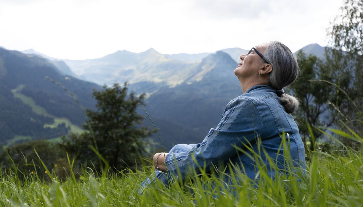 Ältere Frau, sitzt im Gras und schaut in den Himmel.