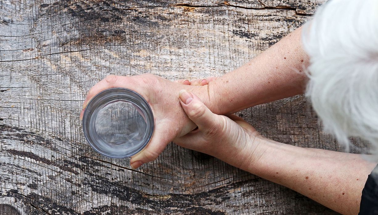 Ältere Frau, hält ein Wasserglas mit zitternder Hand.