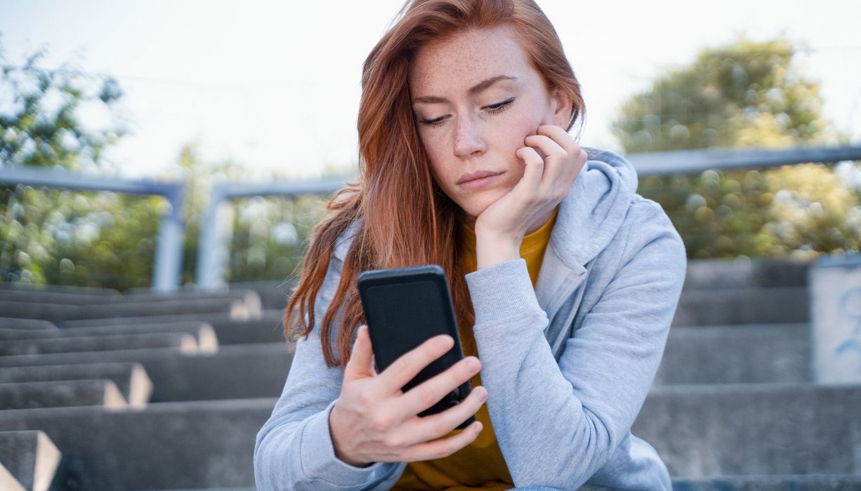 Junge Frau, schaut nachdenklich auf das Handy.