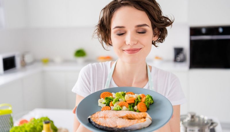 Frau zeigt einen Teller mit Lachs und Gemüse.