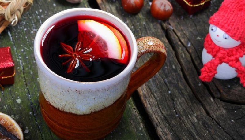 Braun-weißer Keramikbecher mit Glühwein auf dunklem Holztisch. Deko-Schneemann, Nüsse etc. drum herum