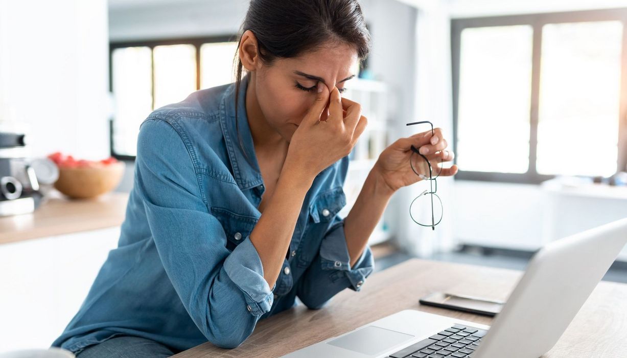 Junge Frau, sitzt vor dem Laptop und hält sich eine Hand an die Stirn.