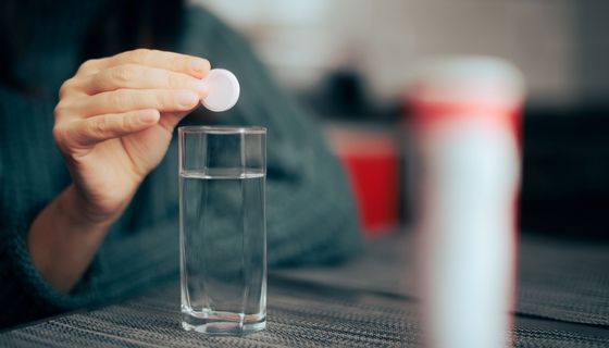 Frau, löst eine Brausetablette in Wasser auf.