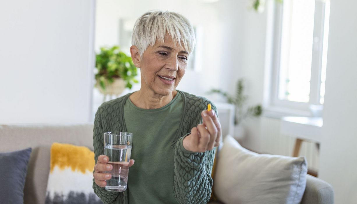 Seniorin, in einer Hand eine Tablette und in der anderen ein Glas Wasser.