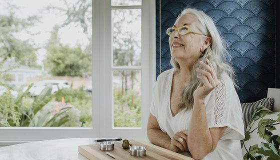 Seniorin sitzt im Bett und raucht einen Joint. Vor ihr liegt auf einem Brettchen ein weiterer sowie ein Bollen Cannabis.