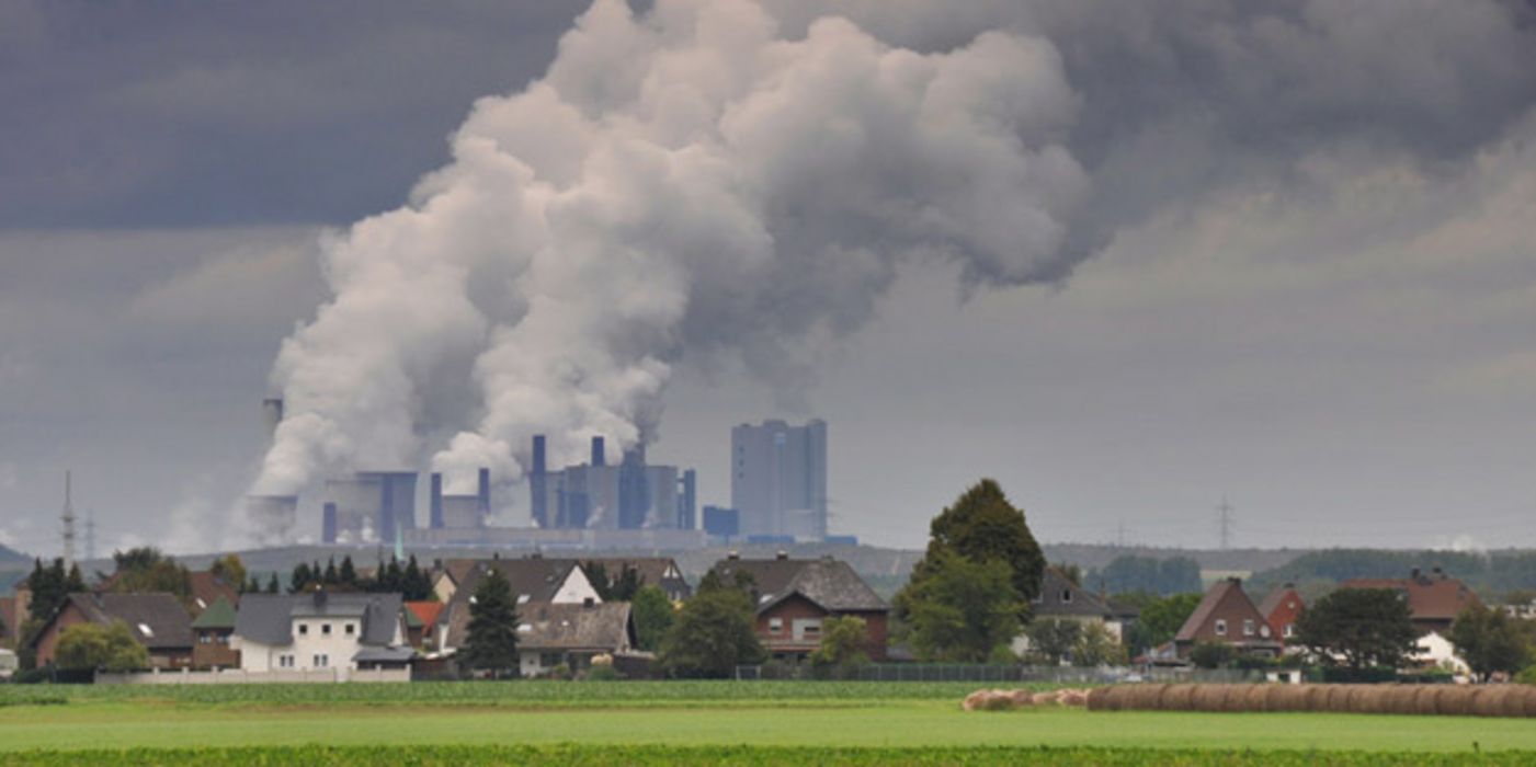 Großes rauchendes Kraftwerk. Davor ein kleines idyllisches Dorf.