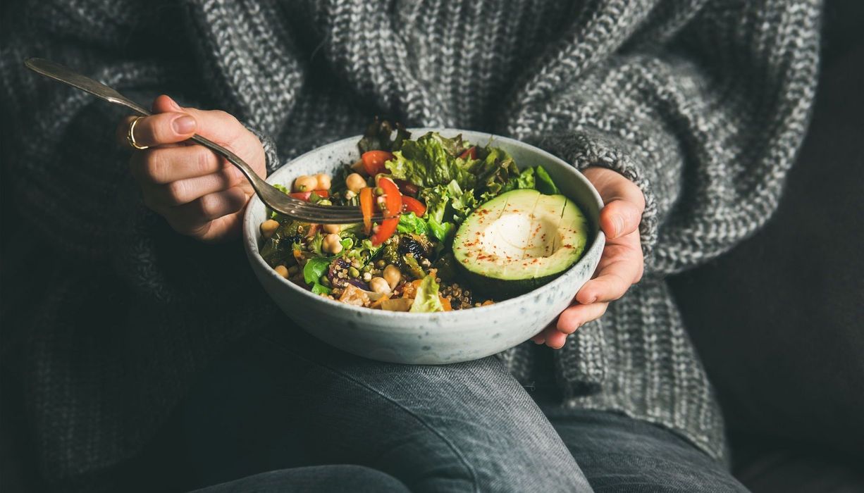 Frau mit dunklem Pullover und einer Schale Salat.