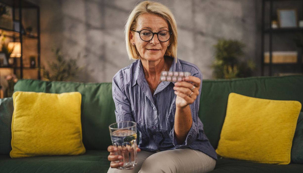 Frau, hält eine Packung Tabletten und ein Glas Wasser in der Hand.