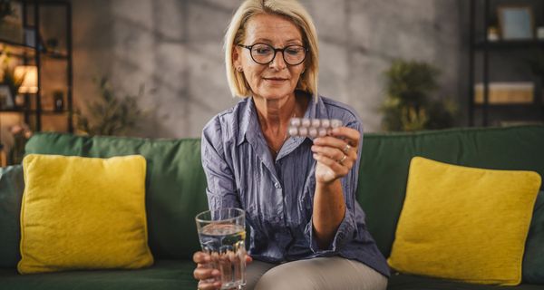 Frau, hält eine Packung Tabletten und ein Glas Wasser in der Hand.