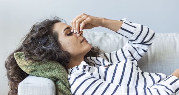 Junge Frau, liegt auf einer Couch und hält eine Hand an den Kopf.