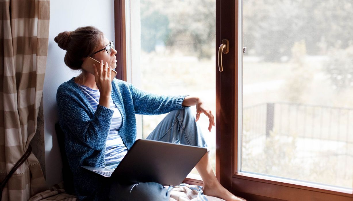 Frau schaut mit Handy am Ohr aus dem Fenster.