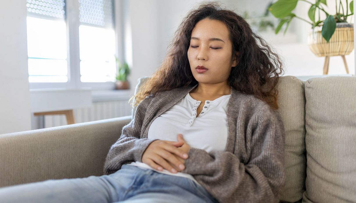 Junge Frau, liegt mit Bauchschmerzen auf der Couch.