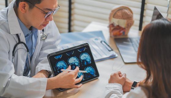 Arzt erklärt dem Patienten während einer Konsultation in der Klinik das MRT-Scan auf dem Tablet und hebt Neurologie, Diagnose, medizinische Diskussion, Gesundheitstechnologie, Bildkonzept, professionelle Versorgung hervor.