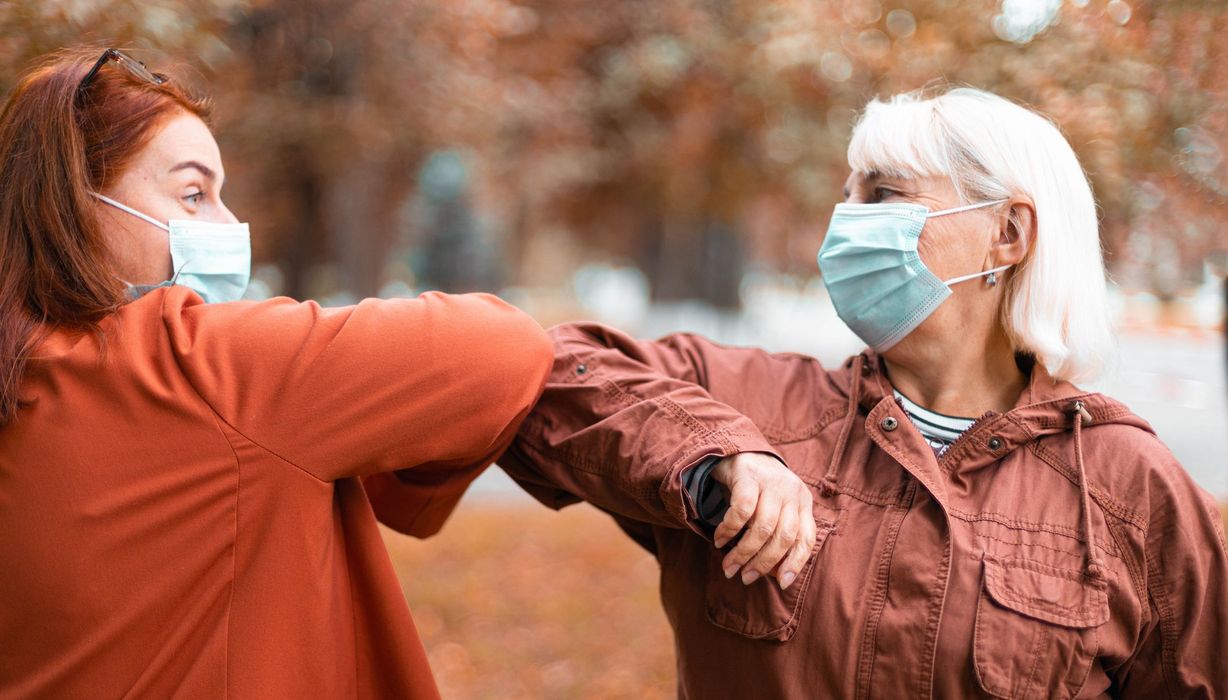 Zwei Frauen mit Maske, begrüßen sich durch ihre Ellenbogen.