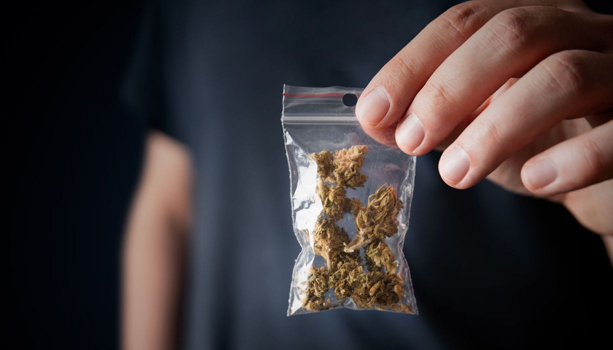 Mann, hält ein Päckchen Cannabis in die Kamera.