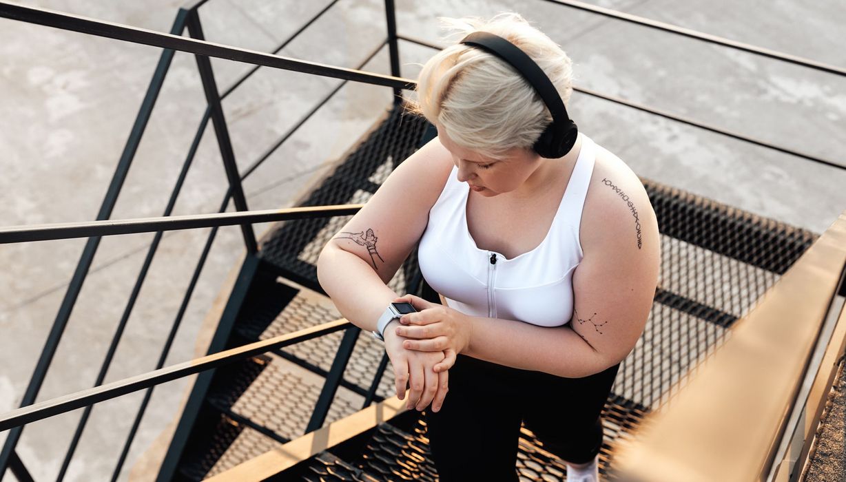 Übergewichtige Frau mit Sportkleidung und Fitness-Armband, läuft Treppen.