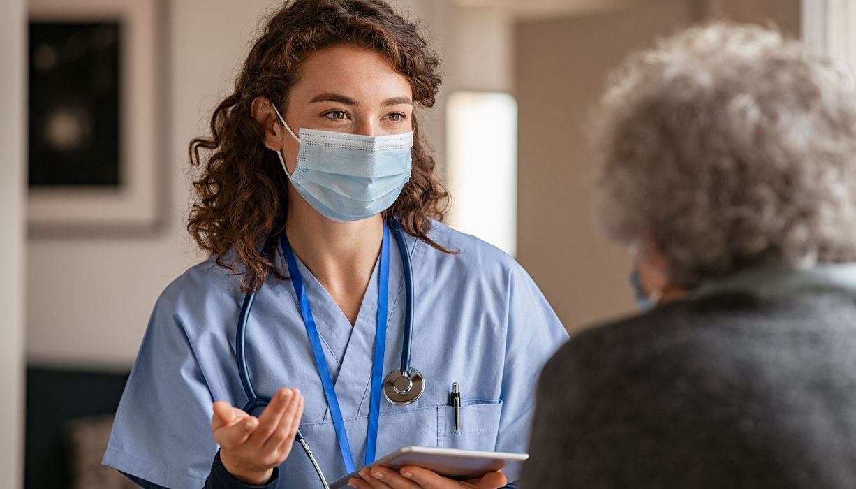 Junge Ärztin mit Mundschutz, spricht mit Patientin.