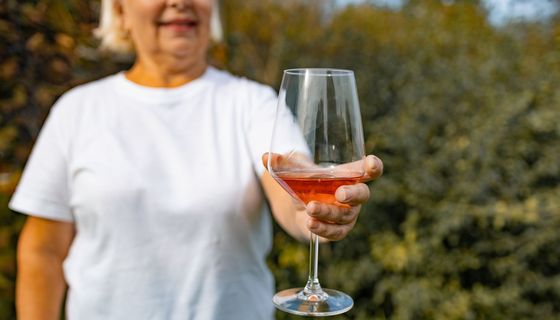 Ältere Frau, hält ein Glas Wein in die Kamera.