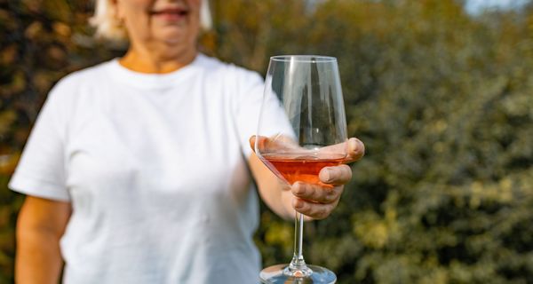 Ältere Frau, hält ein Glas Wein in die Kamera.