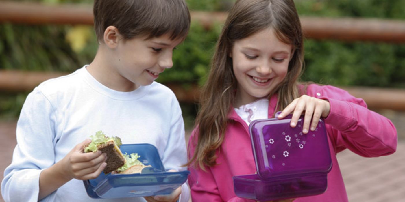 Junge und Mädchen mit Frühstücksbox auf dem Schulhof