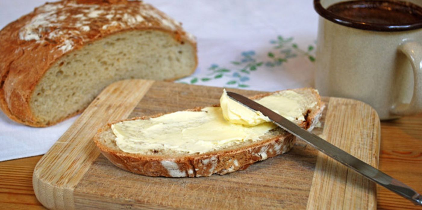 Butterbrot mit Messer auf einem Brett nebst Brotlaib und Kaffeetasse