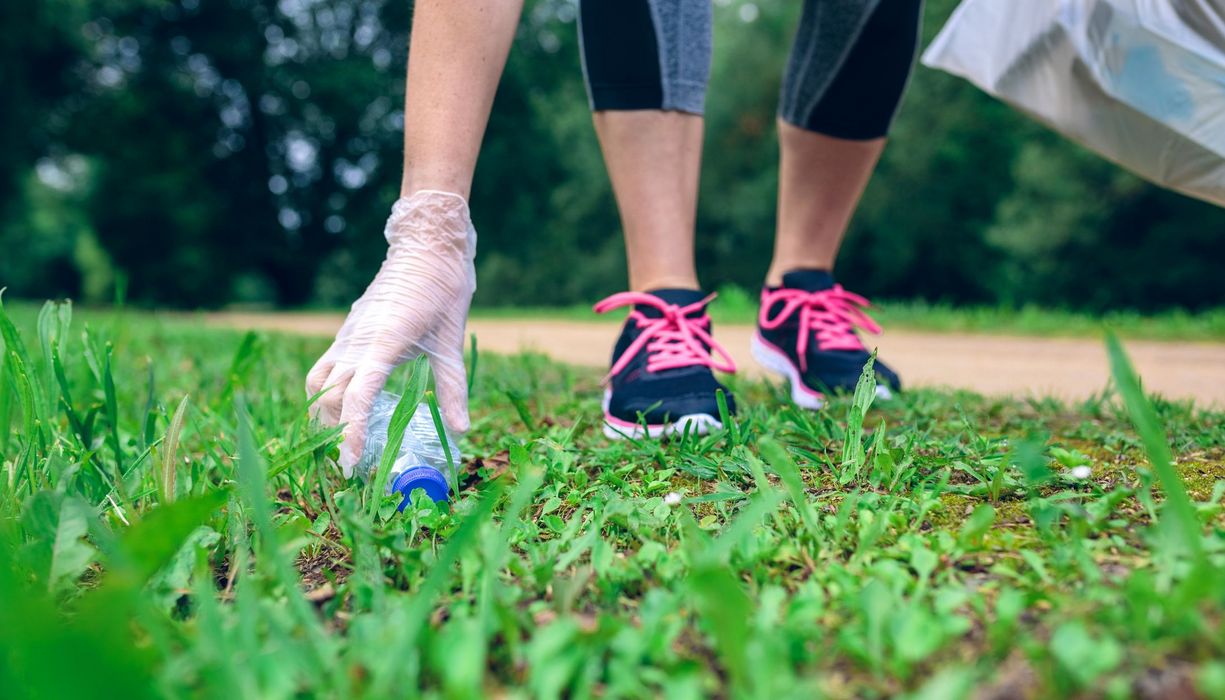 Frau mit Jogginghose, hebt leere Plastikflasche auf. 