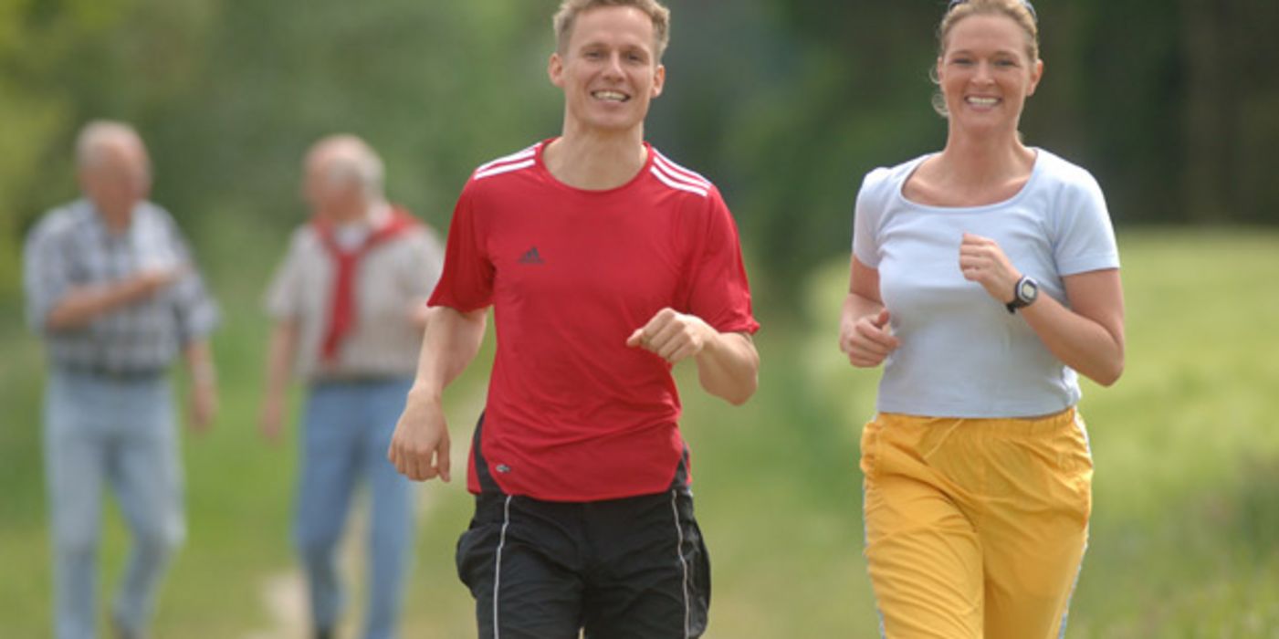 Fröhliche Menschen (Frau, Mann) beim Joggen in grüner Natur