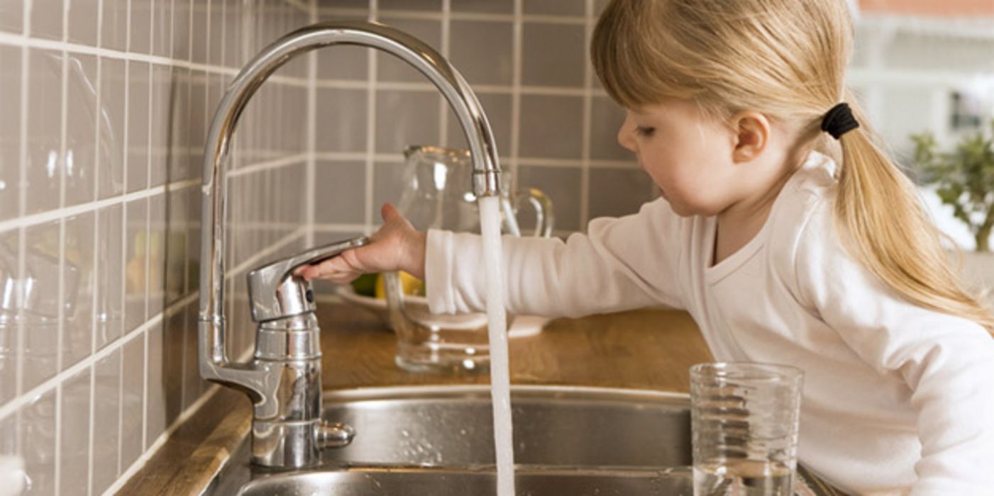 Mädchen dreht Wasserhahn auf.