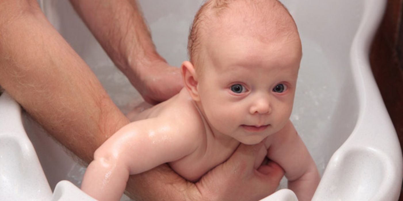 Erwachsener wäscht Baby in einer Wanne mit klarem Wasser