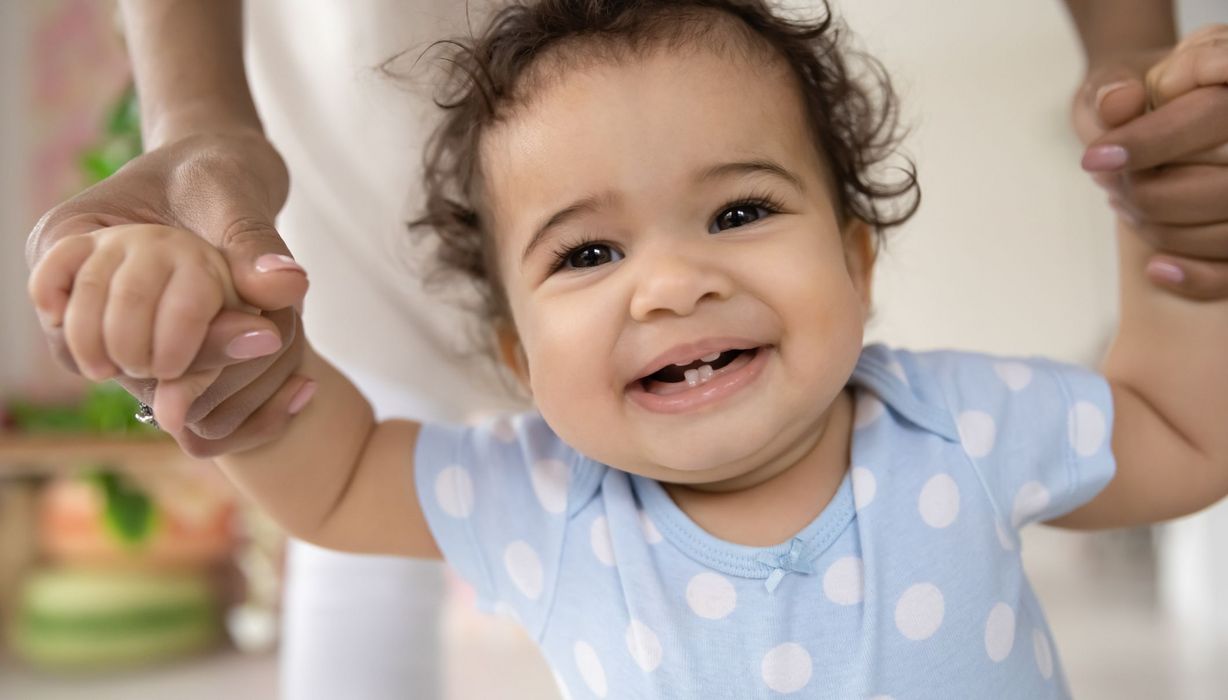 Baby, lächelt in die Kamera und zeigt die ersten Zähne.