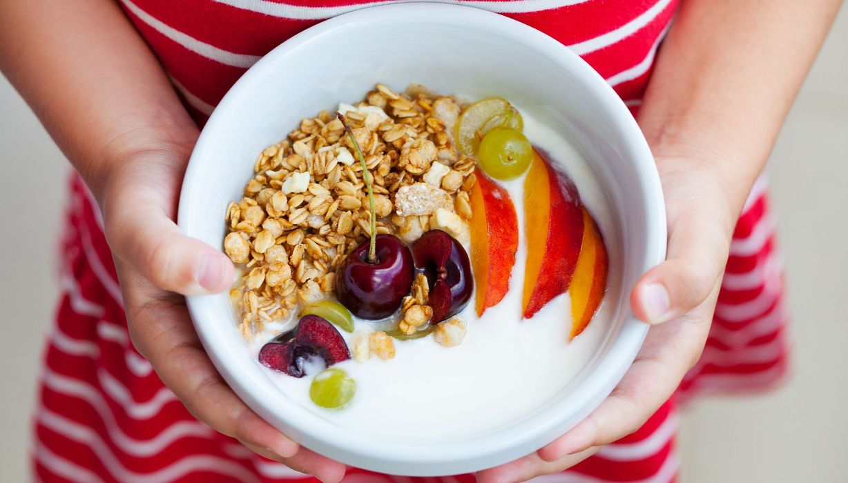 Frau im roten Kleid, hält eine Schale Joghurt mit Müsli und Obst in den Händen.