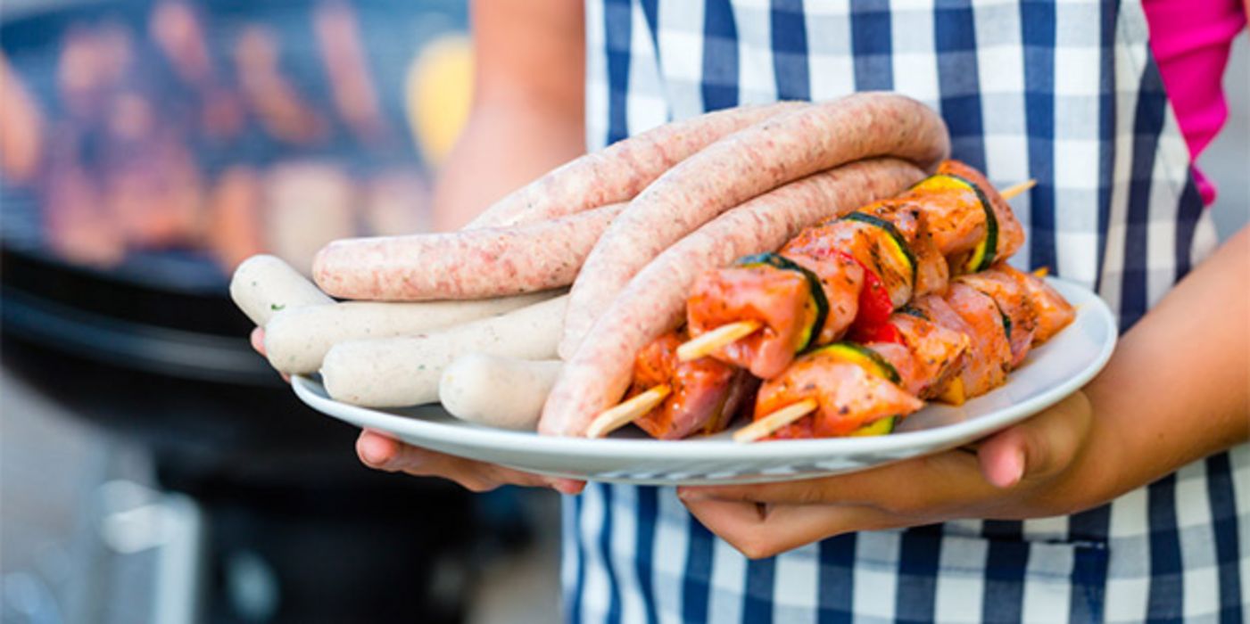 Kopflose Grillmeisterin mit Teller voll mit rohen Fleischspießen und Würsten