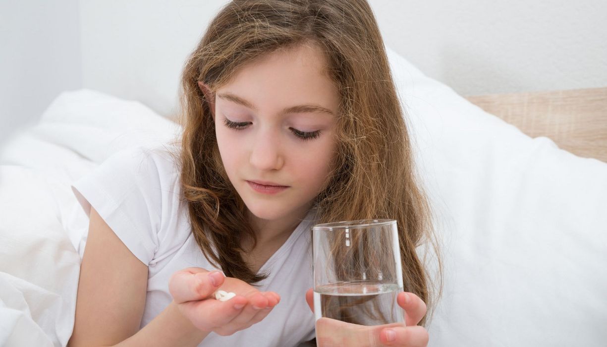 Mädchen mit Wasserglas und Tabletten.