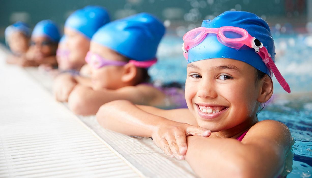 Kinder, mit Haube und Schwimmbrille, am Rand des Schwimmbeckens.