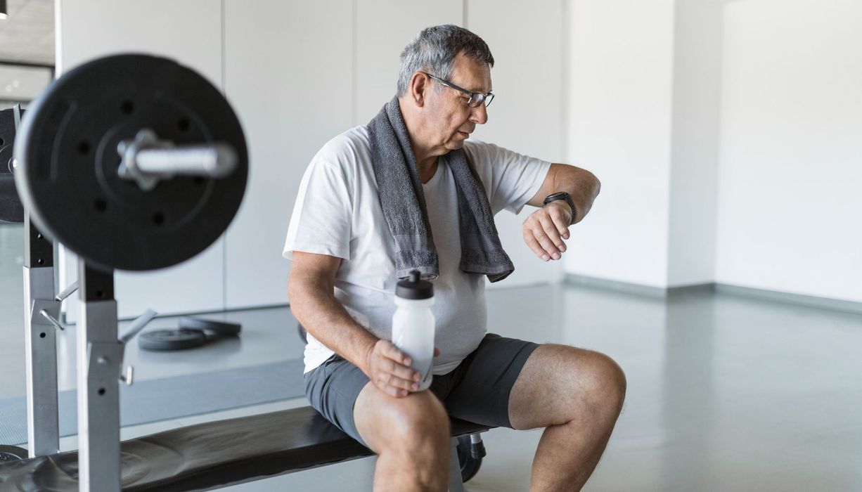 Älterer Mann beim Fitness, schaut auf seine Smartwatch.