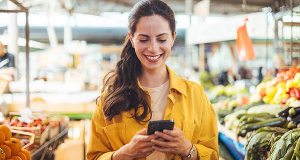 Frau, steht im Supermarkt und schaut auf ihr Smartphone.